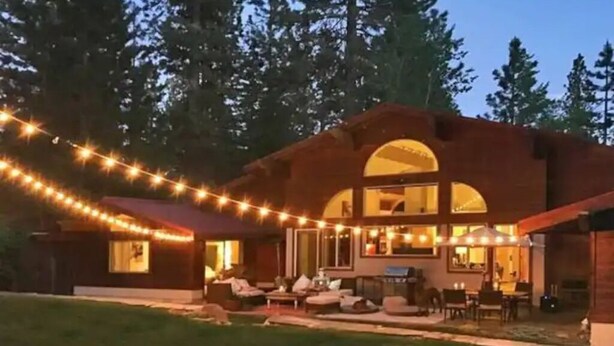 Una casa con un amplio ventanal de arco, mobiliario exterior y luces colgantes.