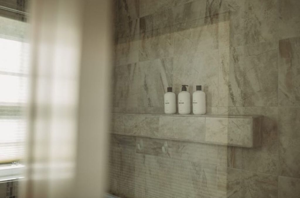 A bathroom with a marble wall and a shelf holding three bottles.