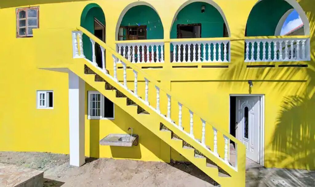 Un edificio amarillo con una escalera que lleva a un nivel superior, una ventana pequeña y una puerta.