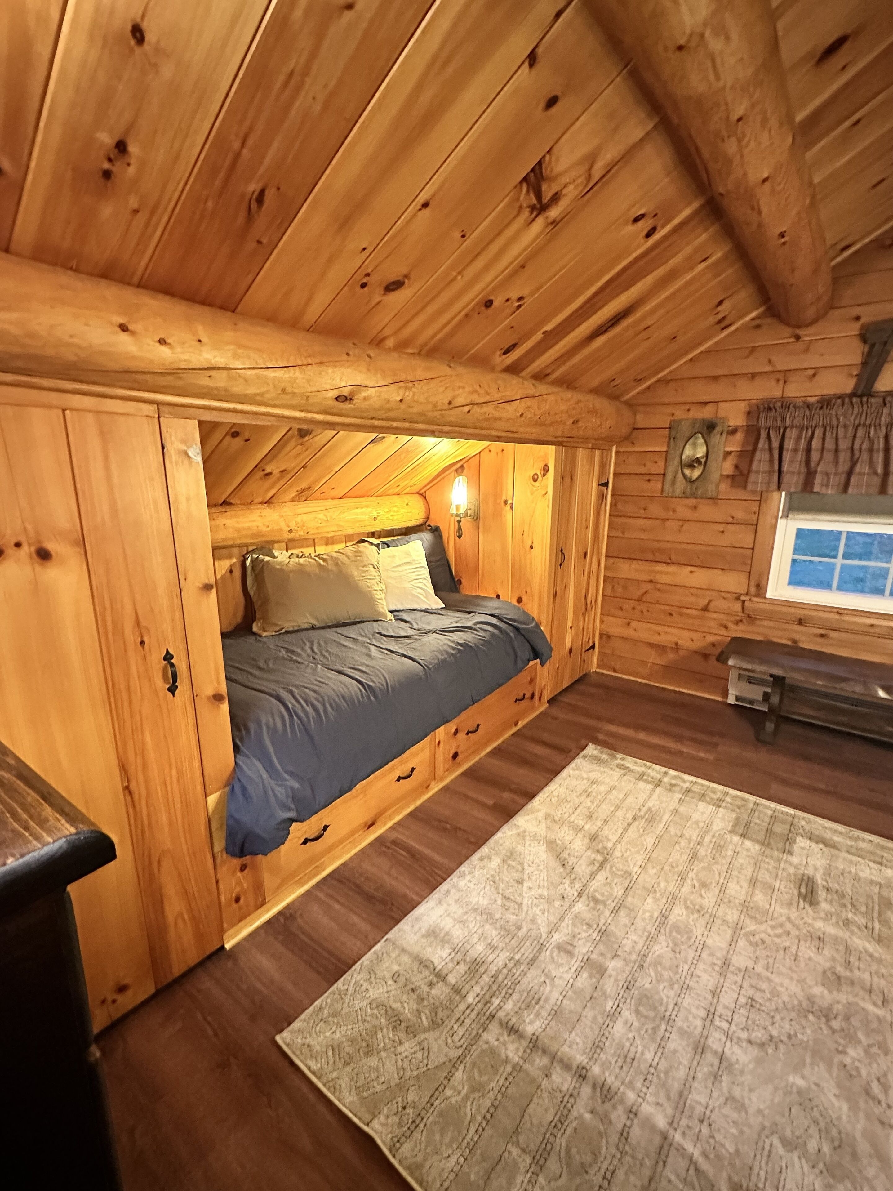 Een knus slaapkamer in een chalet met een hoogslaper, houten wanden en een klein raam.