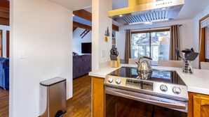 Una cocina moderna con estufa de acero inoxidable, horno empotrado y campana extractora. Hay una ventana con cortinas y vistas al exterior.
