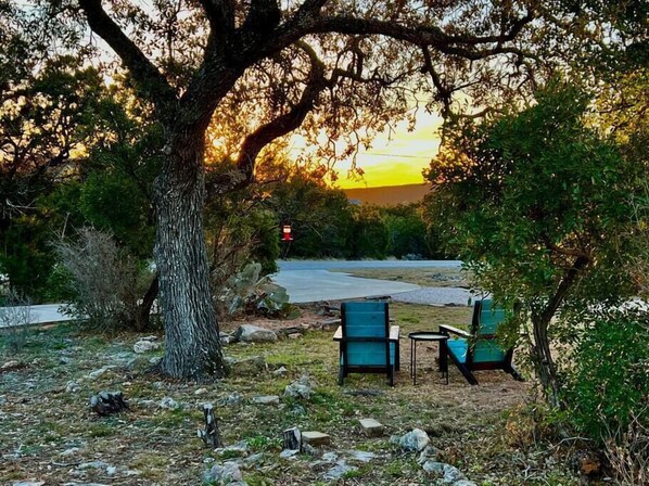 A serene outdoor seating area with two chairs and a table, surrounded by trees and a sunset view.