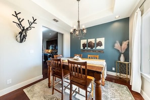 A dining room with a wooden table, chairs, and a chandelier. There are wall-mounted deer antlers and a sign that reads "HOW-GREAT THOU ART". - Hilltop Home: Canyon Lake~ Sleeps 12 •Gameroom •Firepit •1 Acre •RV/Boat Parking (Comal County)
