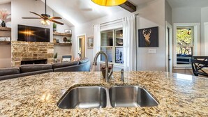 A kitchen with granite countertops, a double sink, a stone fireplace, and a ceiling fan. - Hilltop Home: Canyon Lake~ Sleeps 12 •Gameroom •Firepit •1 Acre •RV/Boat Parking (Comal County)