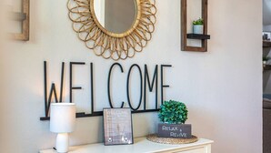 Una pared con un cartel que dice 'WELCOME', un espejo, una lámpara y una planta pequeña.