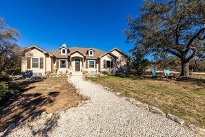 A two-story house with a front porch, a driveway, and a large tree to the right.