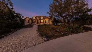 A two-story house with a gravel driveway leading to a front door, surrounded by trees and cacti. - Hilltop Home: Canyon Lake~ Sleeps 12 •Gameroom •Firepit •1 Acre •RV/Boat Parking (Comal County)