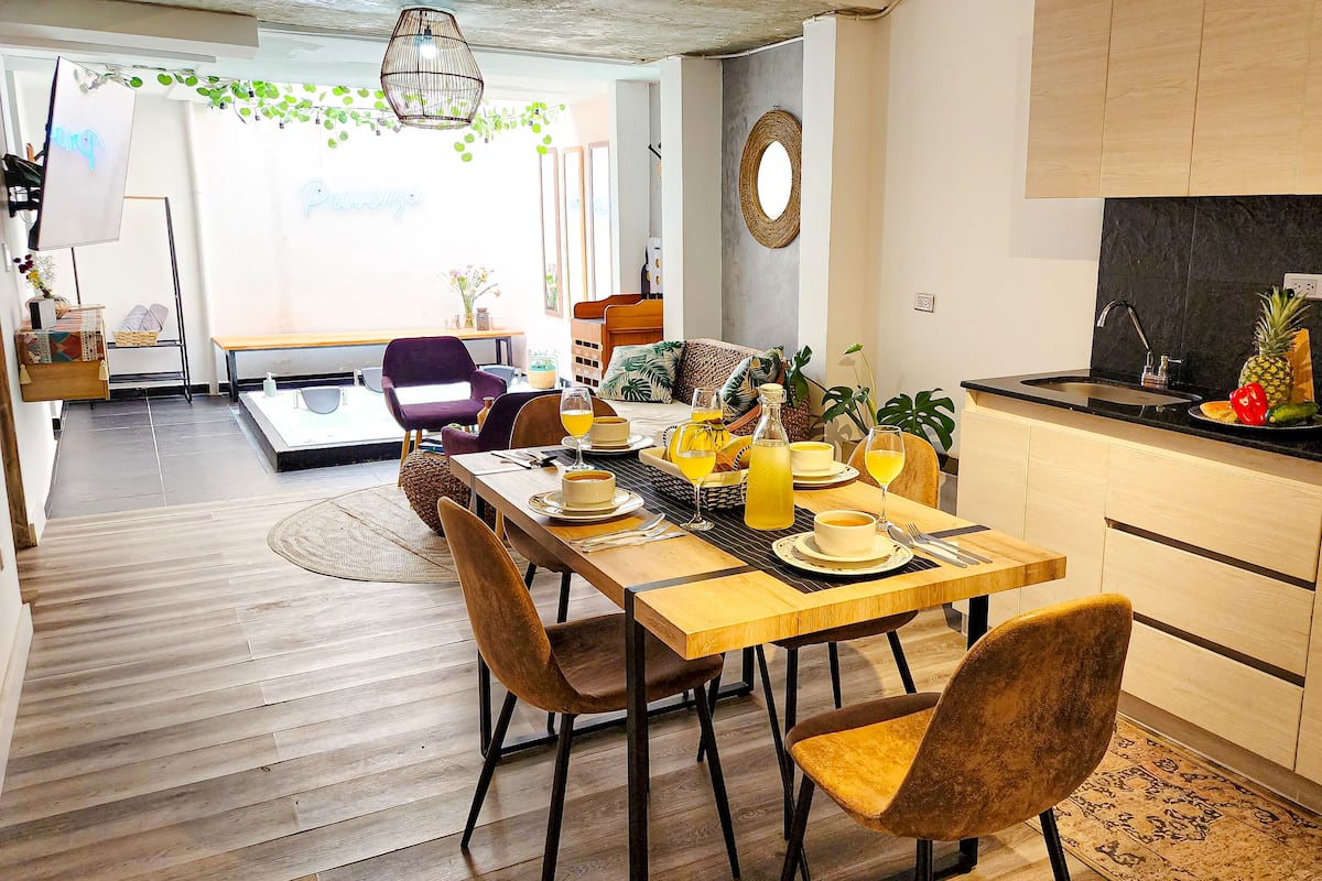 A modern kitchen with a dining area, wooden flooring, and a view to the living room.