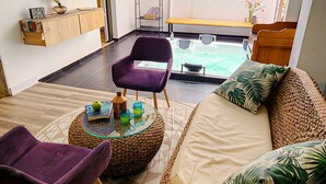 A cozy room with a sofa, a purple chair, a round table with drinks, a TV, and a view of the outdoors. - Town House Jiwa in Provenza (Medellín)