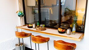 A kitchen with a wooden bar stool seating area, a window with a view of the kitchen, and a shelf with various kitchen items. - Town House Jiwa in Provenza (Medellín)