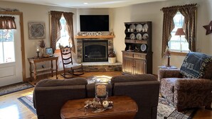 Un salon chaleureux avec une cheminée, un téléviseur et une table basse agrémentée d’objets décoratifs.