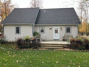 A two-story house with a dark roof, a front porch with a bench, and a small garden area.