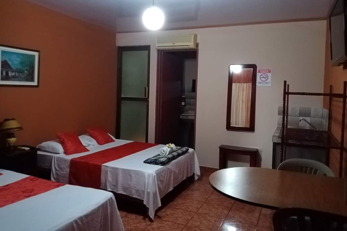 A hotel room with two beds, a dining table, a mirror, and an air conditioning unit.