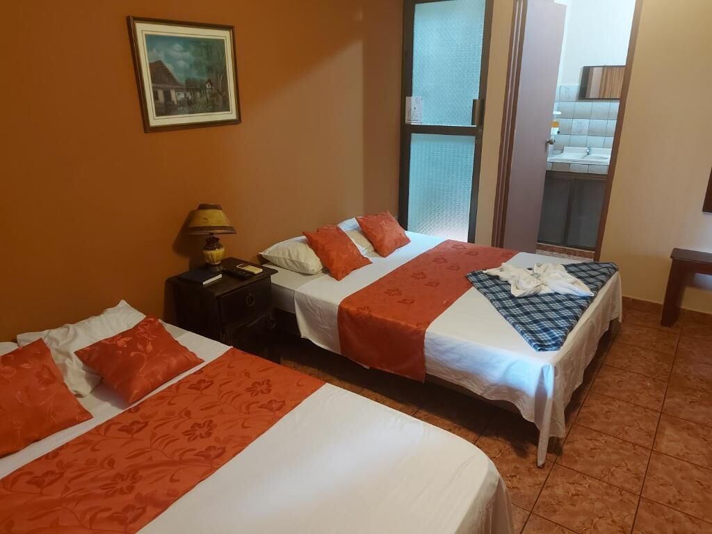 Habitación de hotel con dos camas, una mesita de noche, una lámpara y ventana con vista a un edificio.