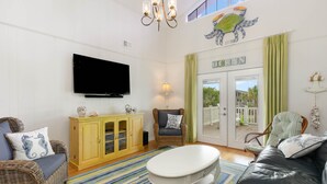 A living room with a flat-screen TV, wicker furniture, a white coffee table, and a view of the outdoors through a glass door. - 4 BDRM CANAL HOUSE WITH LARGE OUTDOOR LIVING SPACE (Ocean Isle Beach)