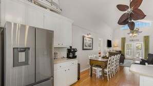 A modern kitchen with stainless steel appliances, a dining area with white chairs, and a ceiling fan. - 4 BDRM CANAL HOUSE WITH LARGE OUTDOOR LIVING SPACE (Ocean Isle Beach)