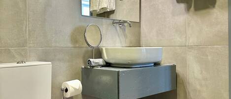 A modern bathroom with a white toilet, a sink with a mirror, and two towels hanging on a towel rack.