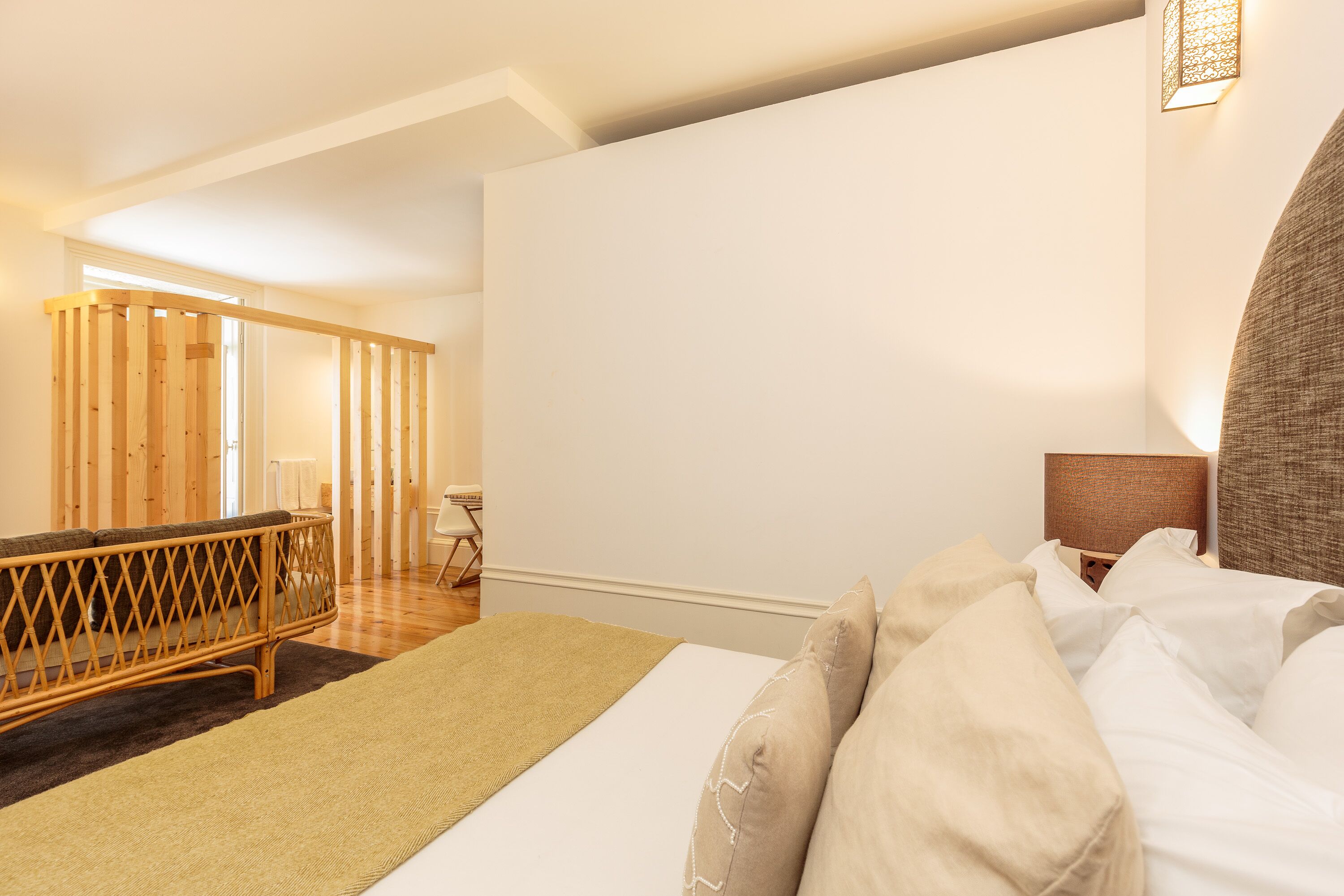 A hotel room with a bed, a wooden partition, a small table, and a lamp.
