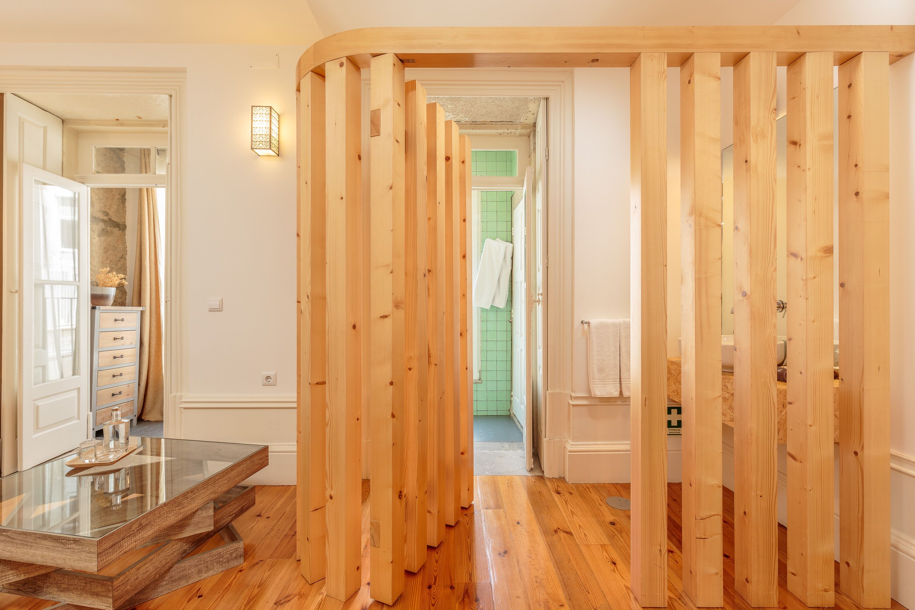 A hallway with wooden partitions, a glass table, and a view into a bathroom with green tiles.