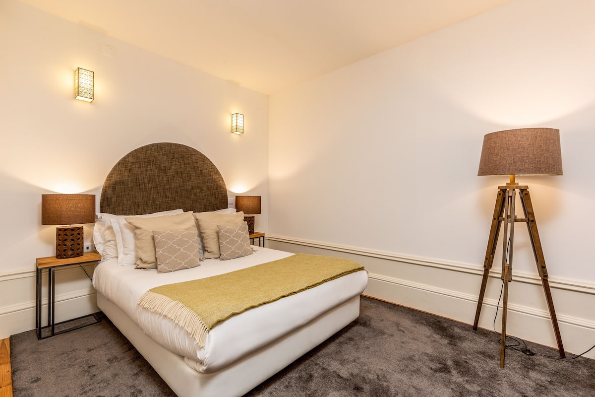A neatly arranged bedroom with a large bed, two bedside lamps, a floor lamp, and a wall-mounted light fixture.