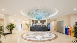 Un hall d’hôtel avec un comptoir d’accueil central, un grand lustre décoratif et un motif circulaire sur le sol.