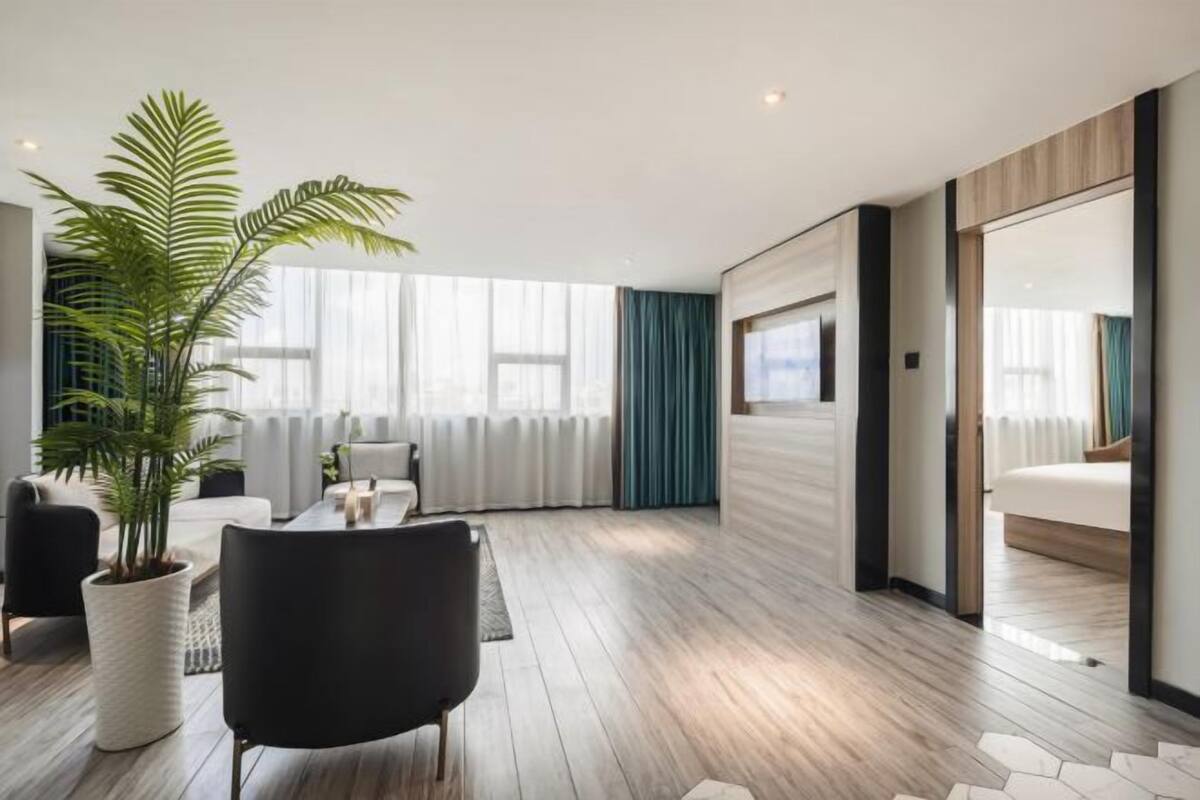 Habitación de hotel moderna con un ventanal grande, una planta en maceta, una silla negra y una cama.