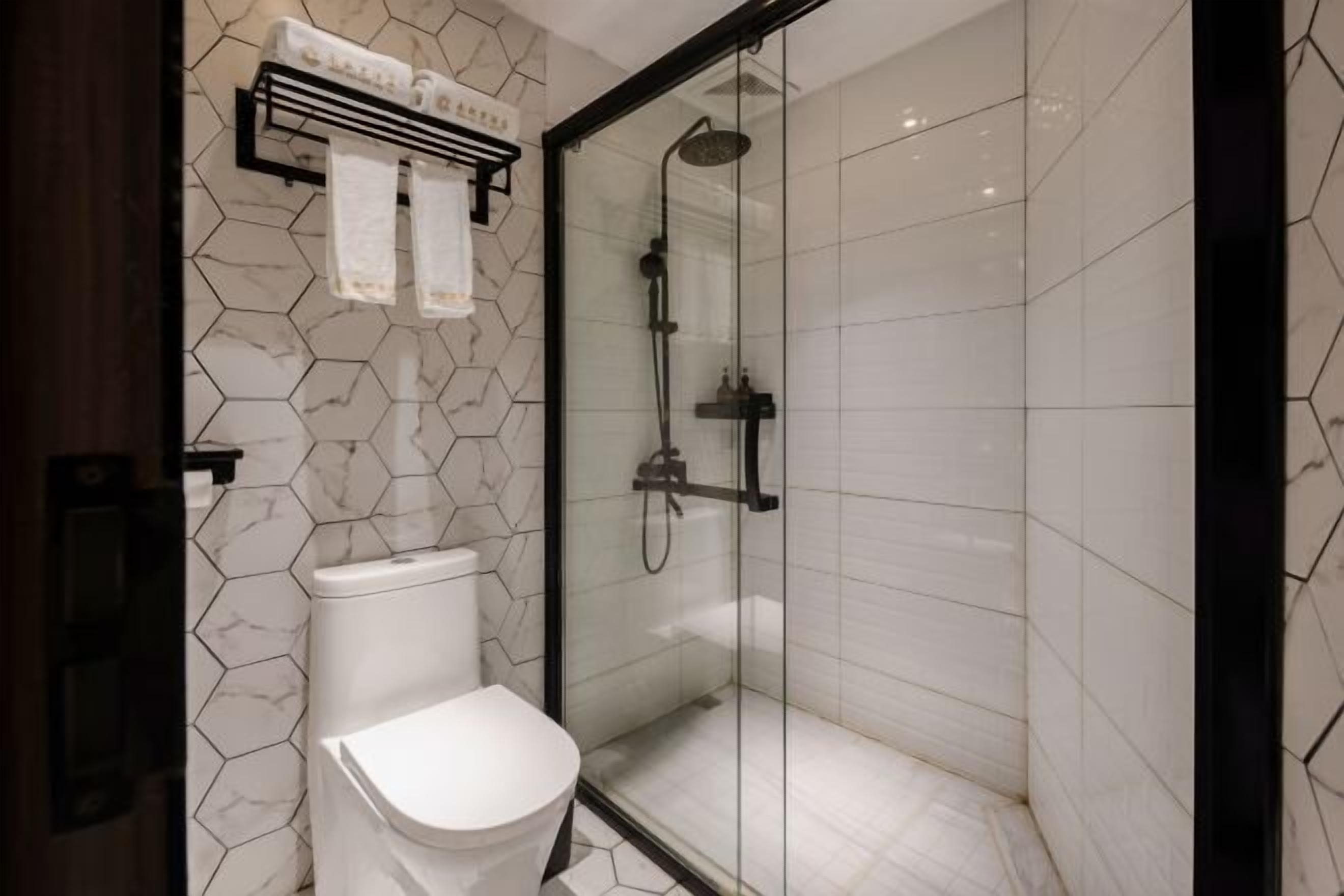 A modern bathroom with a glass-enclosed shower, a white toilet, and a towel rack with two towels.