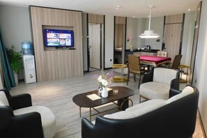 A hotel room with a flat-screen TV mounted on the wall, a dining area with a table and chairs, and a seating area with sofas. - Nangulee Hotel (Hepu)