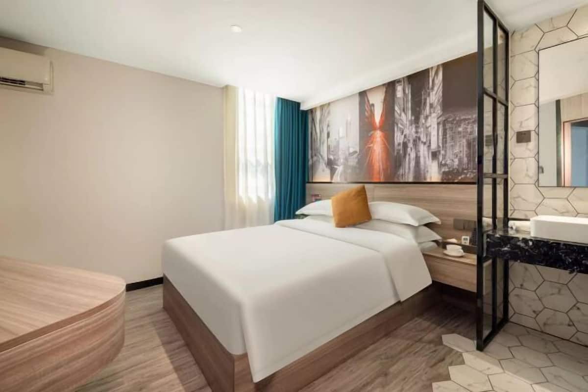 Habitación de hotel con cama, mesita de noche, baño con espejo y lavabo, y un cuadro abstracto grande en la pared.