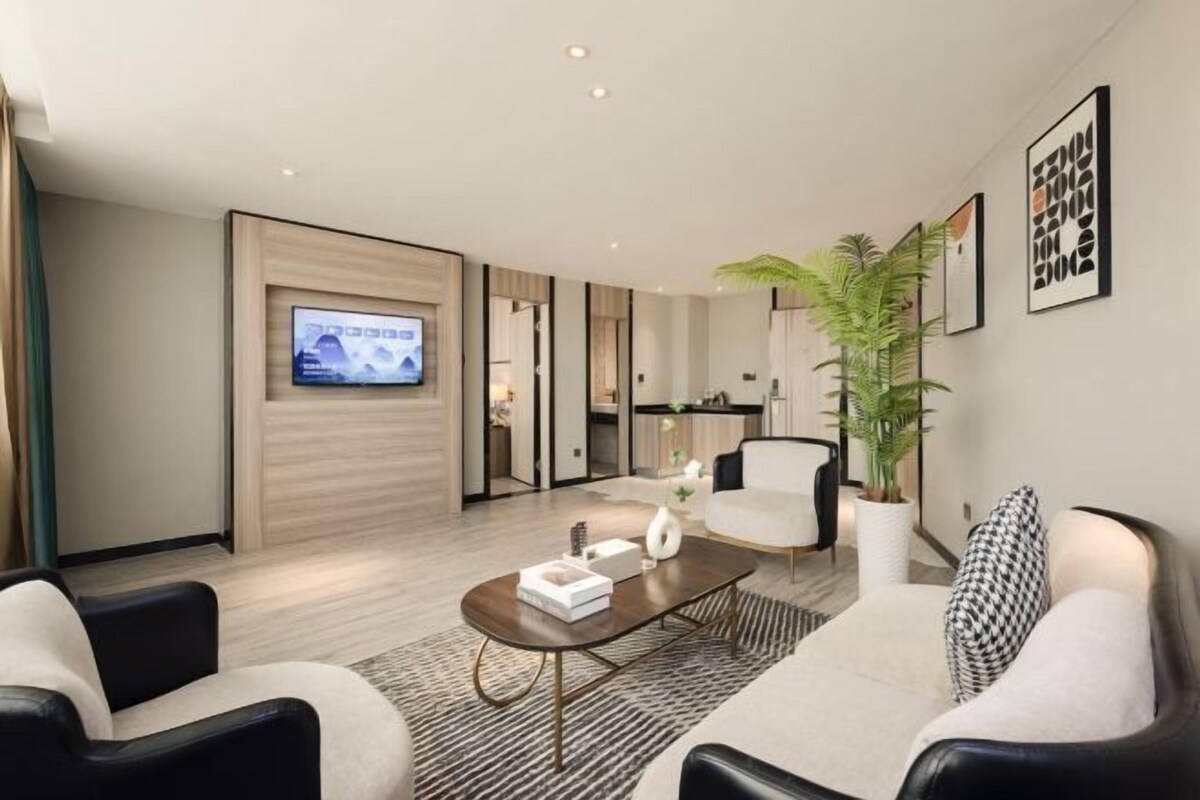 A modern living room with a flat-screen TV, a coffee table, two sofas, a potted plant, and framed artwork on the wall.