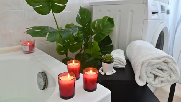 Un baño con una bañera, tres velas encendidas, una planta en maceta y una toalla enrollada sobre una mesa negra.