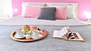 Una bandeja de desayuno ordenada con croissants, una taza y un libro sobre una cama con ropa de cama rosa y gris.