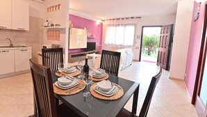 Comedor con una mesa dispuesta para cuatro, cocina con muebles blancos y vistas al exterior a través de un ventanal.