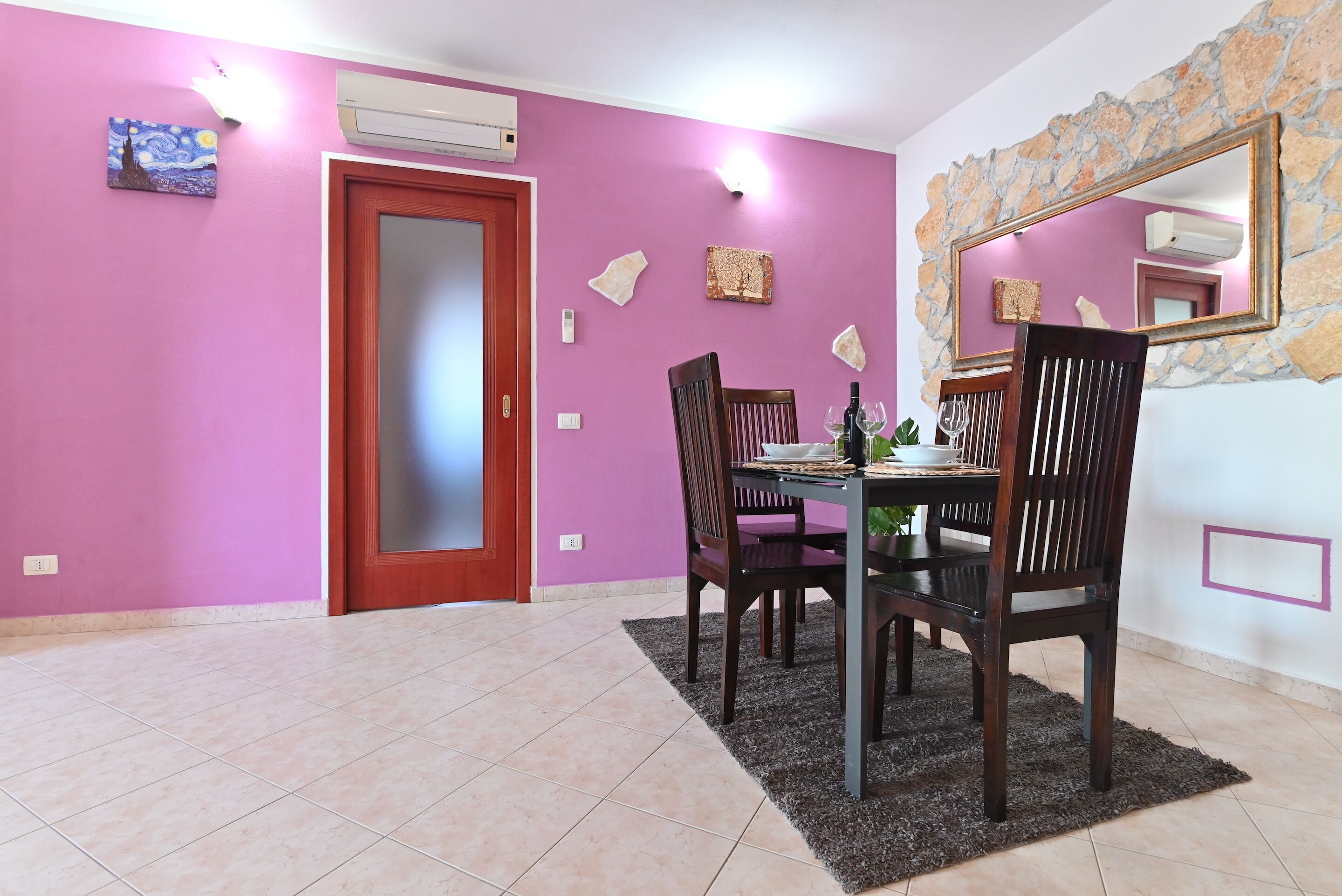 Un coin repas avec une table dressée pour quatre personnes, une porte en bois et un mur de pierre agrémenté d’un miroir.
