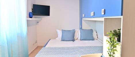 Una habitación de hotel con cama, televisor, planta y baño con cortina de ducha.