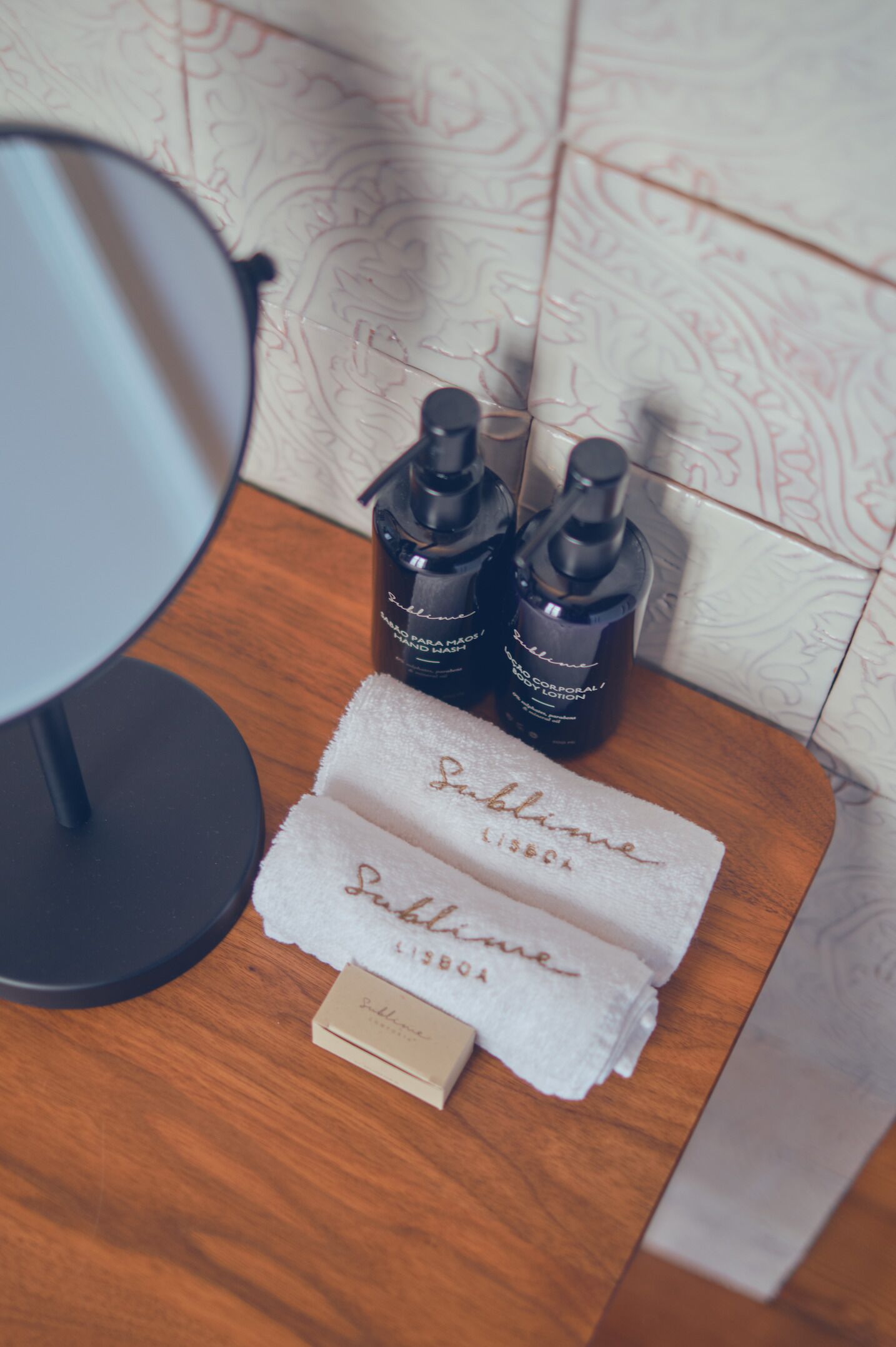 A bathroom vanity with a round mirror, two bottles of lotion, a folded towel, and a small box.