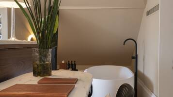 Un baño con bañera, espejo, planta y una mesa con lámpara y libros.