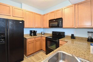 A kitchen with wooden cabinets, a black refrigerator, a microwave, a stove, and a granite countertop.