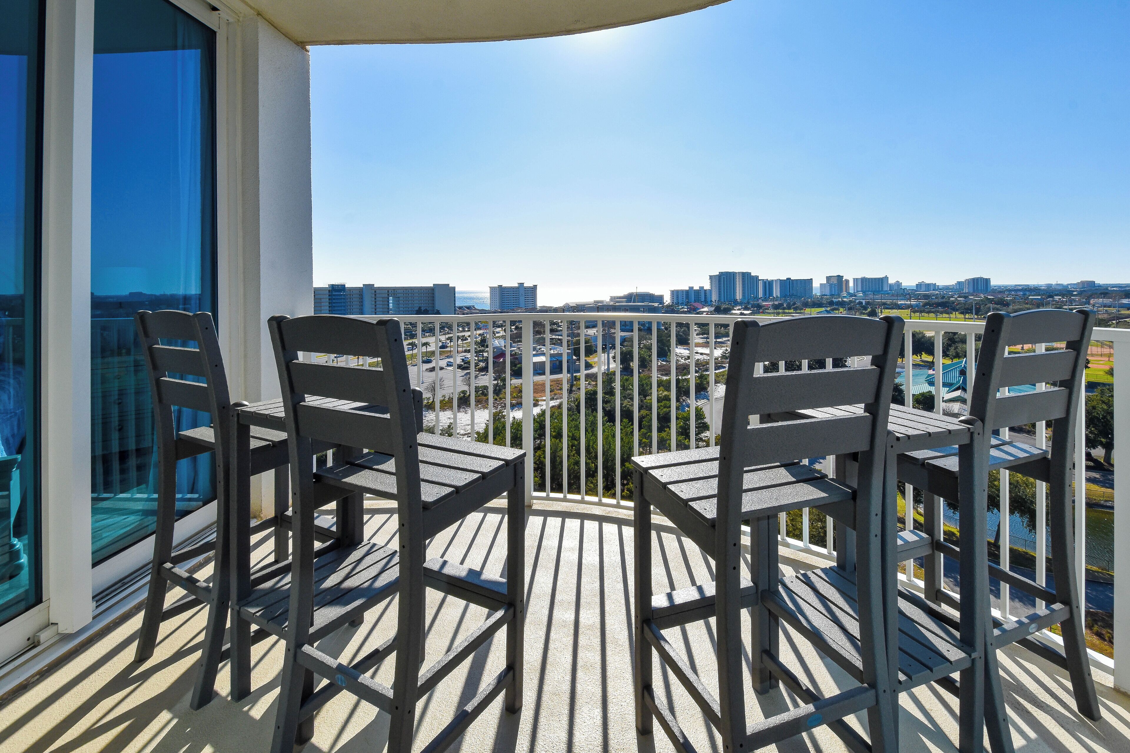 A balcony with four chairs and a table, overlooking a cityscape with buildings and greenery.