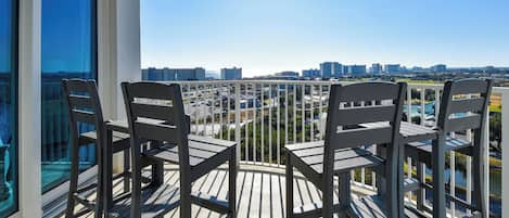 A balcony with four chairs and a table, overlooking a cityscape with buildings and greenery.