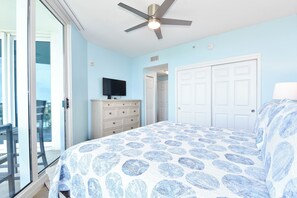Quarto com cama, penteadeira, televisão e ventoinha no teto.