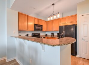 A kitchen with wooden cabinets, granite countertops, a black refrigerator, a microwave, and a coffee maker.