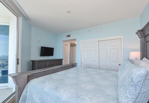 A bedroom with a large bed, a TV mounted on the wall, a wardrobe, and a door leading to another room.