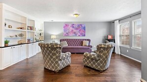 A spacious living room with a purple sofa, patterned armchairs, and a large abstract painting on the wall. - The Tangle by Host Boise - 4500sqft Boise Home| 9 Beds & Dual Master| 85" TV (Boise)