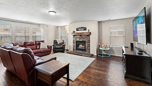 A living room with a fireplace, leather sofa, and a television. - The Tangle by Host Boise - 4500sqft Boise Home| 9 Beds & Dual Master| 85" TV (Boise)