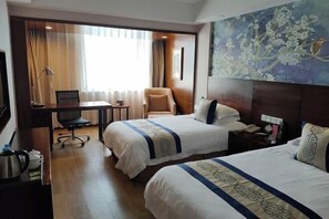 A hotel room with two beds, a desk, a chair, a small table, and a painting on the wall.