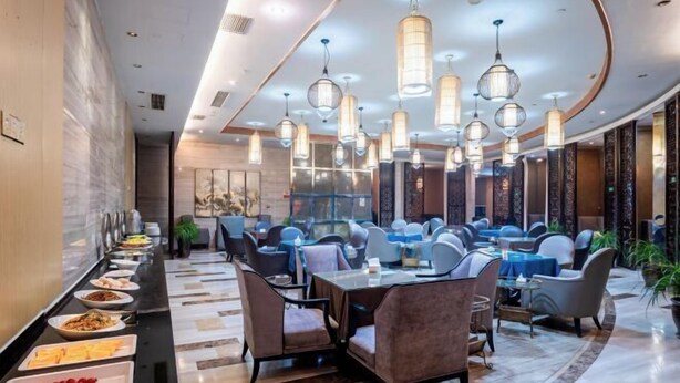 Un hall d’hôtel moderne avec un long buffet, plusieurs espaces aménagés pour s’asseoir et un éclairage décoratif.
