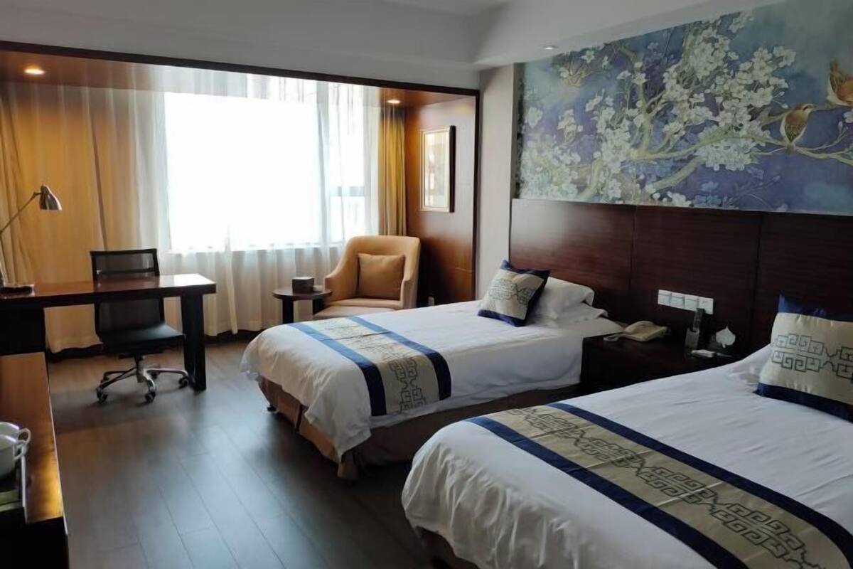 Une chambre d’hôtel avec deux lits, un bureau, une chaise et une grande fenêtre avec des rideaux.