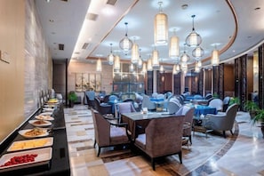 Um hall de hotel moderno com uma longa mesa de buffet, assentos confortáveis e iluminação pendente elegante.