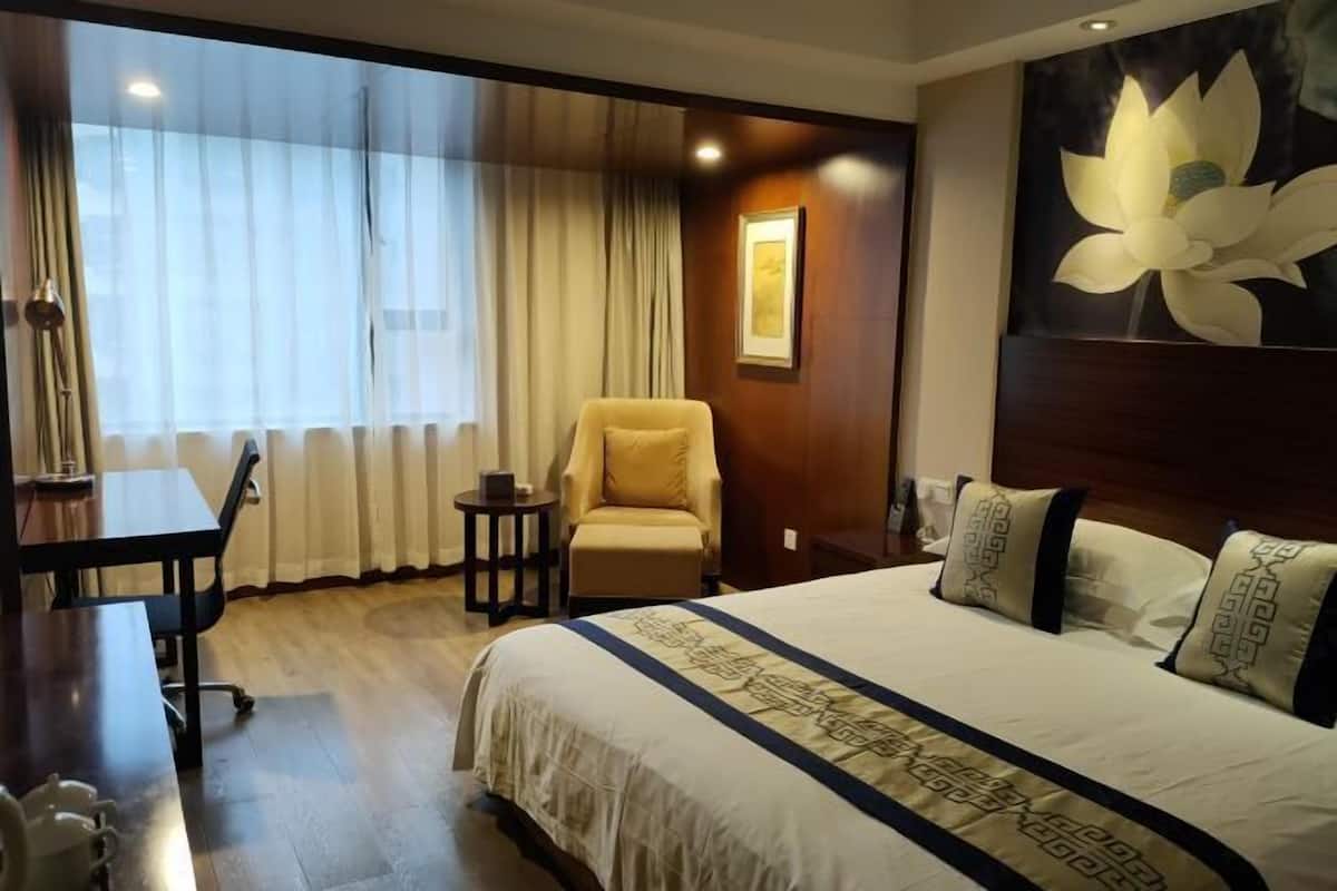 Une chambre d’hôtel avec un grand lit, un bureau, une chaise et une fenêtre avec des rideaux.